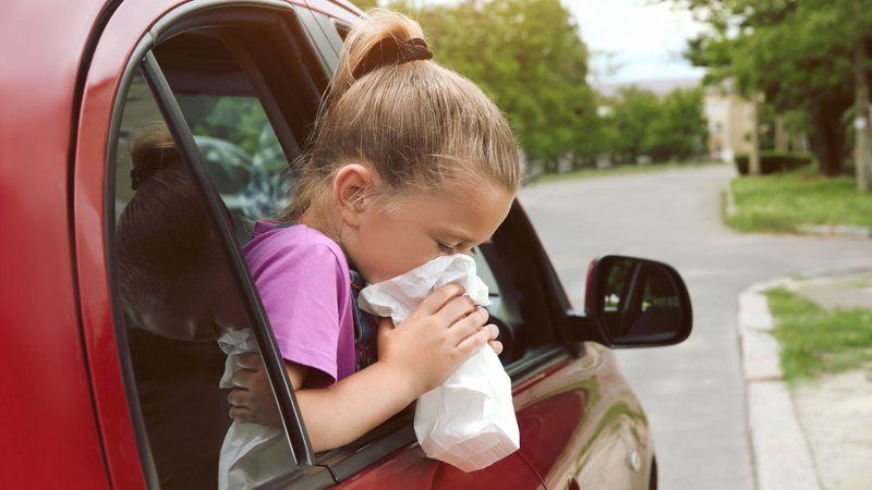 kind hangt wagenziek uit het raam van een rode auto