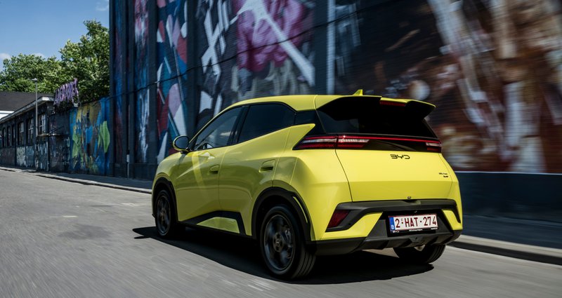 Vue arrière de la BYD Dolphin Surf jaune roulant en ville, devant un mur recouvert de fresques colorées