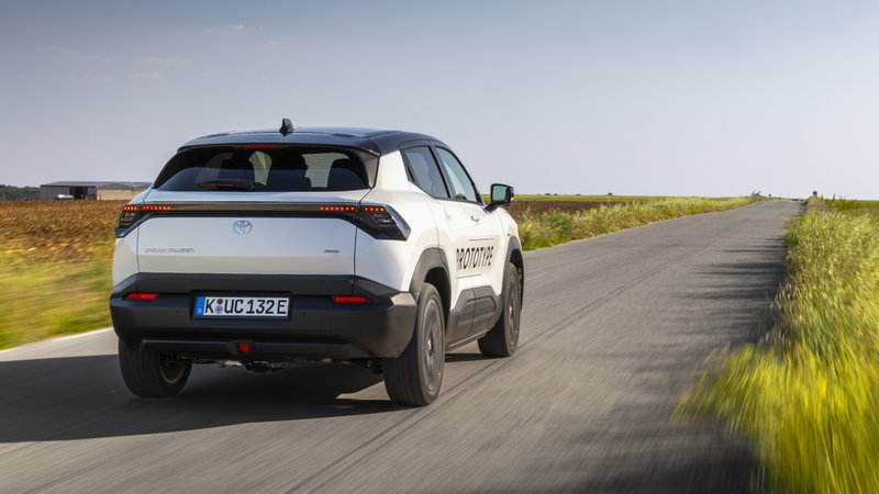 "Vue arrière d’un prototype de SUV électrique blanc, immatriculé en Allemagne, roulant sur une route de campagne bordée de champs. Toyota