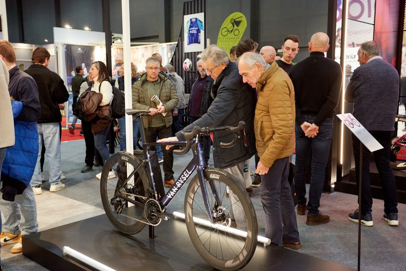 Twee Velofollies bezoekers kijken aandachtig naar een Van Rysel racefiets