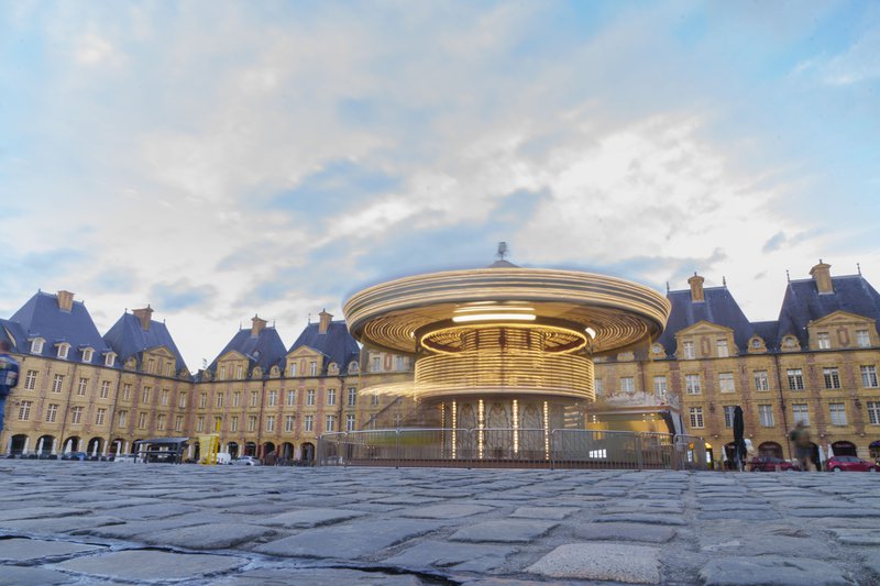 Carrousel sur une place entouré de bâtiments ocres.