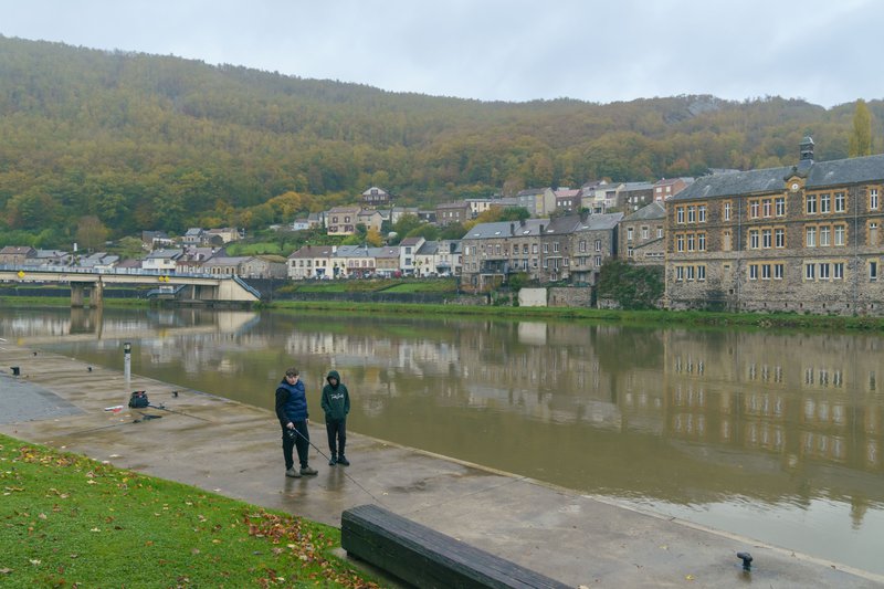 Deux promeneurs sur la rive d'un fleuve en face d'une ville.
