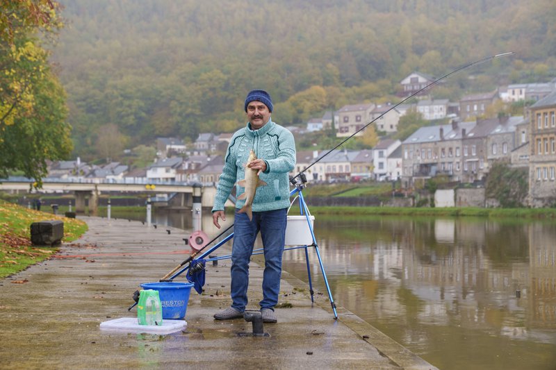 Pêcheur posant avec un poisson au bord d'un fleuve.