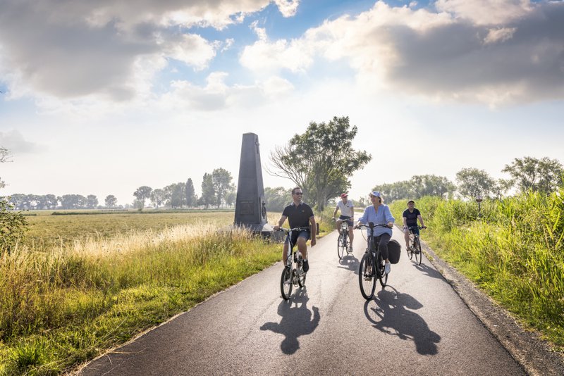 fietsers op een asfaltstrook in de natuur rond de frontsteden, toren op de achtergrond