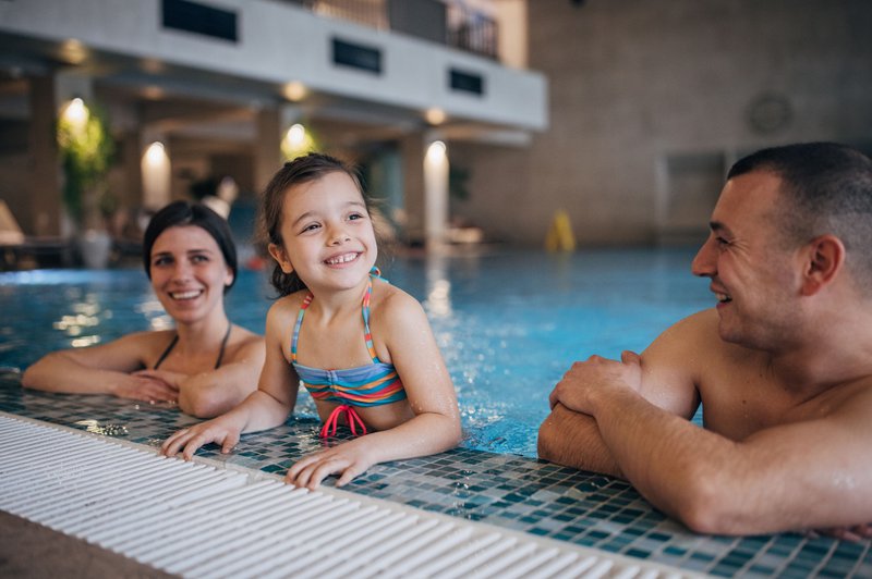 Une piscine dans un hôtel familial, avec un enfant et ses parents au bord du bassin