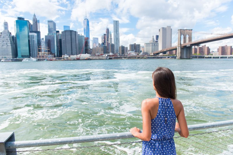 Une jeune fille contemple, de l'autre côté d'une rivière, les gratte-ciel qui se dressent sur la rive opposée