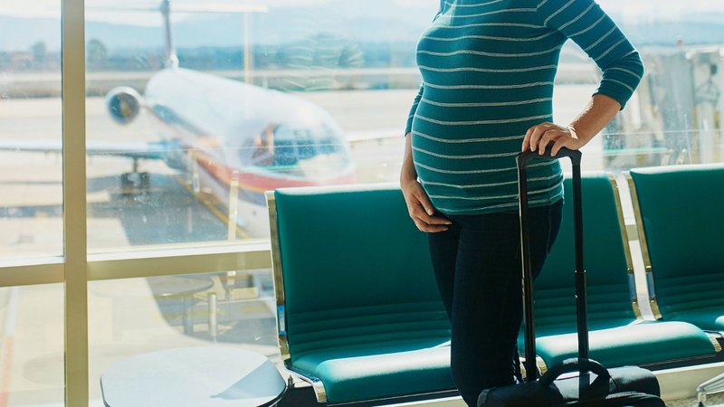 vrouw die zwanger is met trolley in de luchthaven