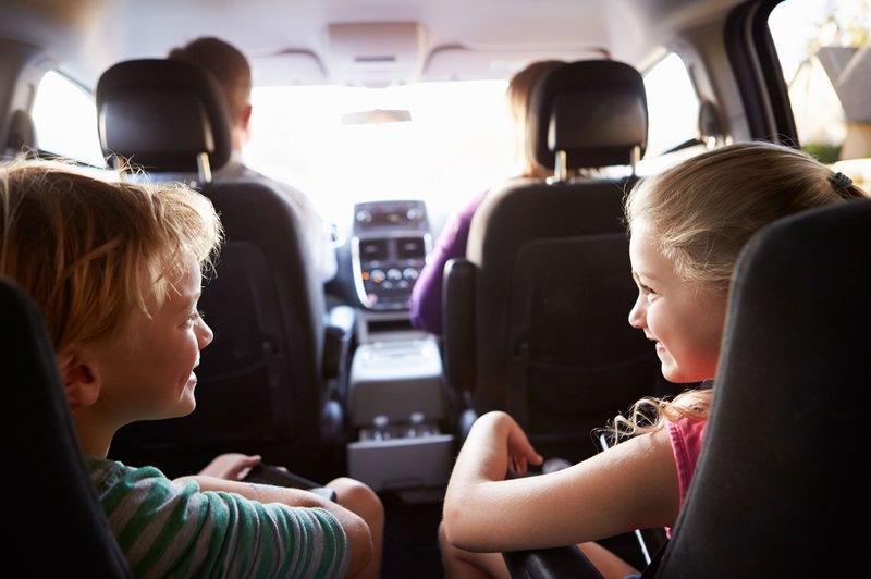 twee kinderen, jongen en meisje, lachend op de achterbank van een auto