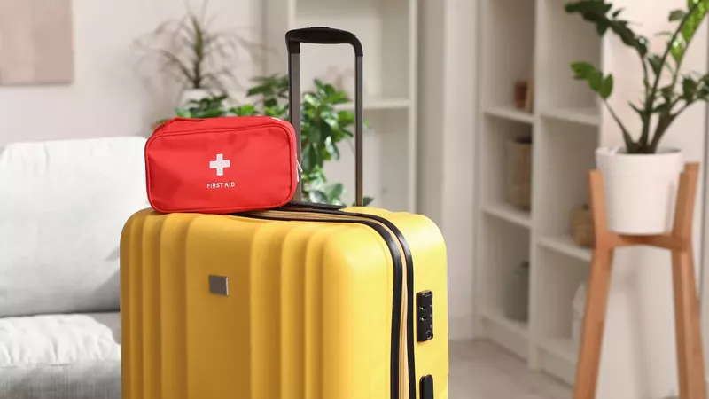 une trousse de premiers secours rouge posée sur une valise jaune dans un salon.