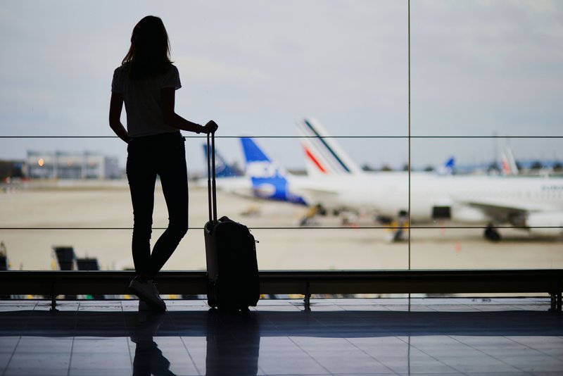 Silhouette d'une personne tenant un bagage à main près d'une vitre dans un terminal d'aéroport
