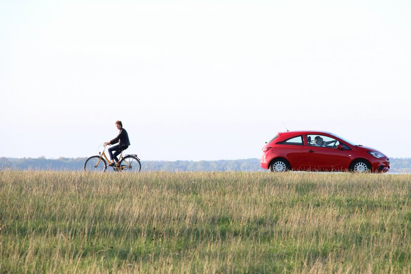 Une voiture et un cycliste se croisent sur une route de campagne.