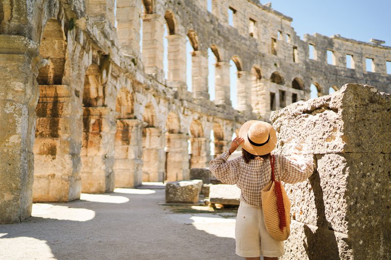 Vrouw met hoed staat te kijken naar het Colosseum in Pula, Kroatië
