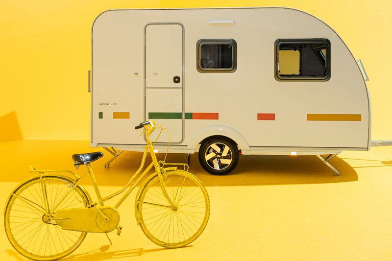 Lichtgewicht caravan op een gele achtergrond met een gele fiets vooraan in beeld