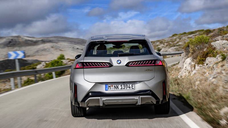 BMW iX3 vu de l’arrière en circulation sur une route sinueuse, avec feux arrière à signature lumineuse marquée.