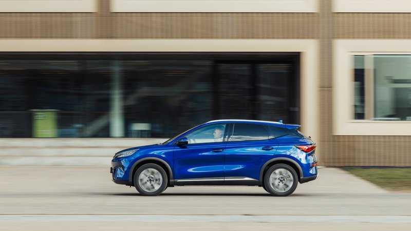 BYD Atto 3 Evo bleu vu de profil, en circulation devant un bâtiment moderne.
