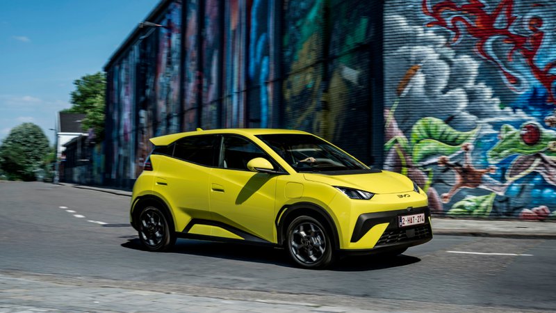 BYD Dolphin Surf électrique jaune en mouvement dans une rue urbaine avec des graffitis en arrière-plan.