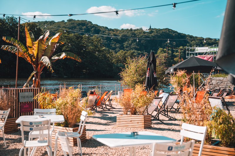Kiezelstrand aan de Maas in Namen met stoelen, ligzetels, exotische planten en parasols.