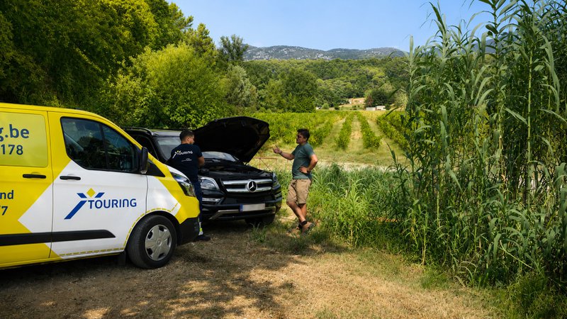 Un dépanneur et son véhicule de dépannage aide un automobiliste en panne en pleine nature.