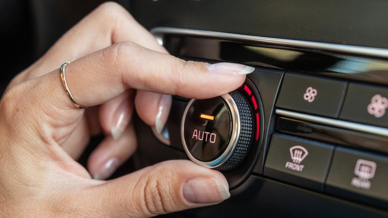 Hand die de automatische airconditioning op het dashboard van een auto instelt.