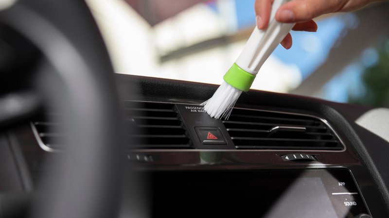 De ventilatieroosters van een auto schoonmaken met een klein borsteltje.