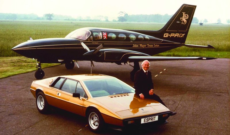 Colin Chapman posé sur une Lotus Esprit dorée, devant un avion privé John Player Special aux couleurs Team Lotus.