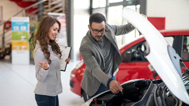 Verkoper toont een klant de motor met open motorkap in de showroom.