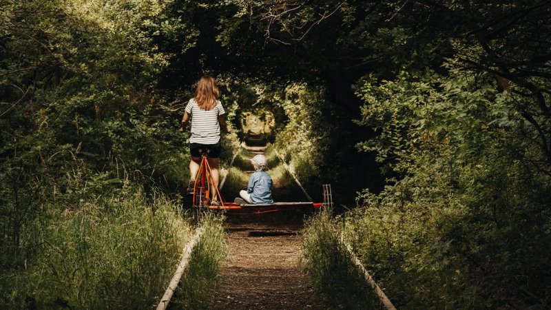 ouder met kind fiets op speciaal voertuig op spoorweg dwars door een bos