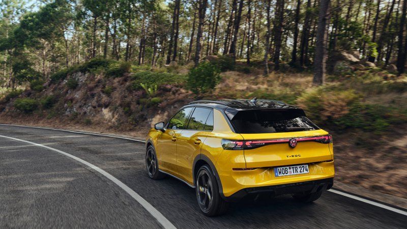 Volkswagen T-Roc jaune vu de l’arrière roulant sur une route forestière, SUV compact au design dynamique