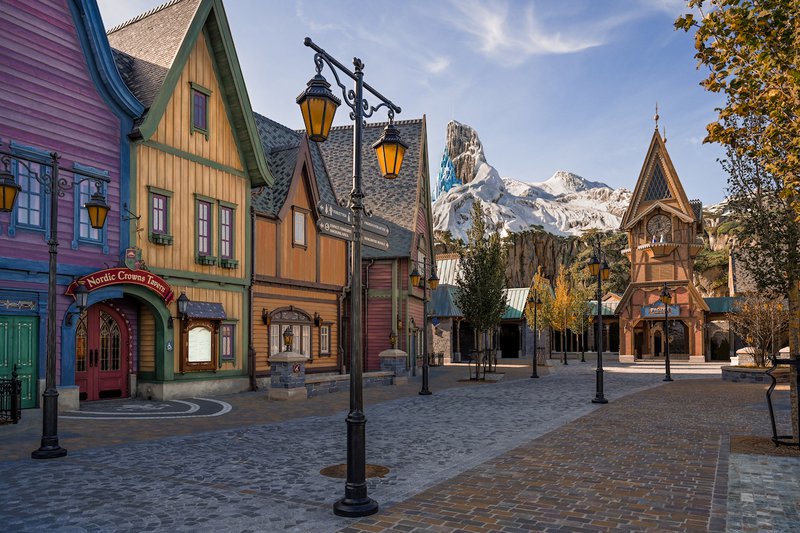 Décor de parc d'attractions avec des maisons en bois sur fond de montagnes enneigées.