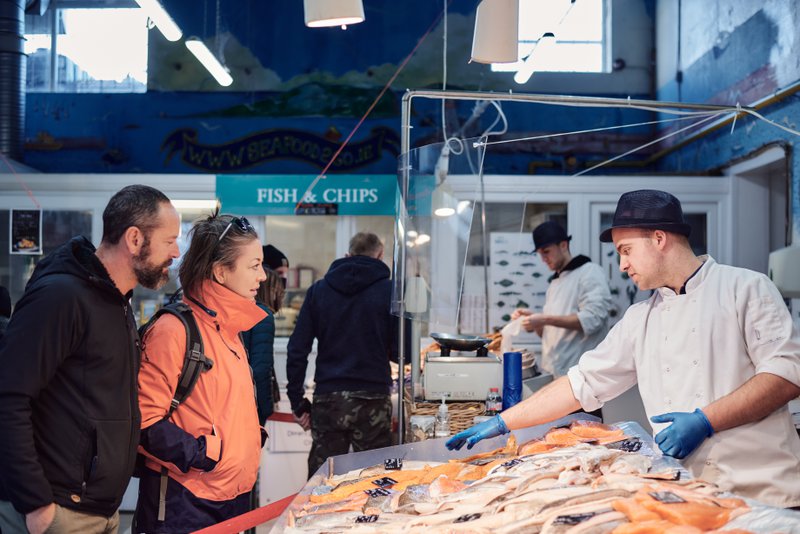 Poissonnerie en Irlande, vendeur proposant du poisson frais et deux clients examinant le poisson.