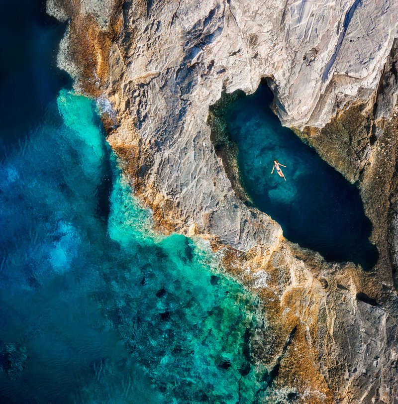 Een luchtfoto op een vroege zomerochtend van een vrouw die zich ontspant in het natuurlijke zeewaterzwembad genaamd “Dragon's Eye” in de baai van Brbinjscica op het eiland Dugi Otok, Kroatië.