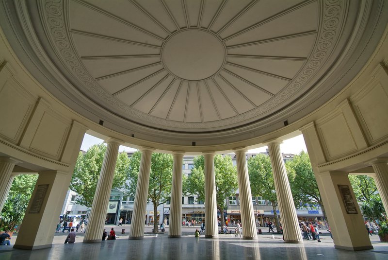 Pavillon avec des colonnes blanches à Aix-la-Chapelle qui donne sur une rue bordée d'arbres.
