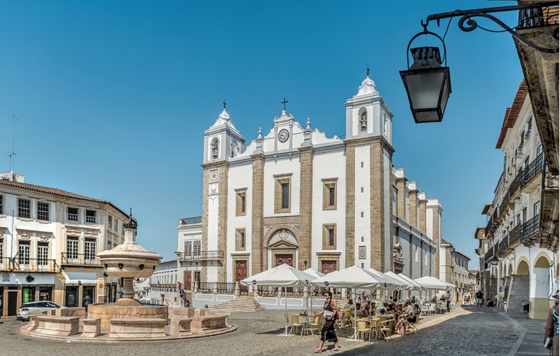 Witte gevel van een Portugese kerk op een zonnig plein met een fontein.