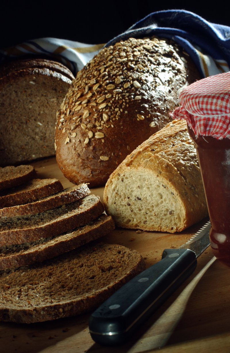 Du pain coupé en tranches, un pot de confiture et un couteau à pain à l'avant-plan.