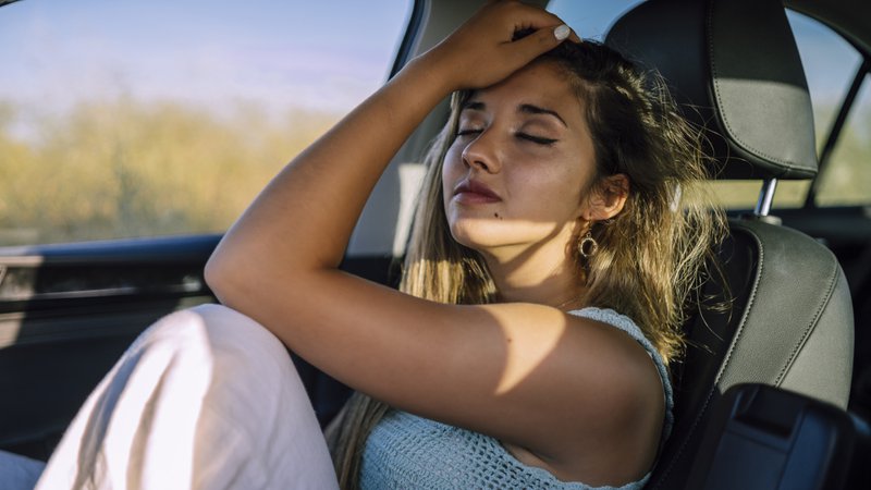 Een jonge vrouw die last heeft van de hitte op de voorstoel van een auto die in de zon geparkeerd staat.