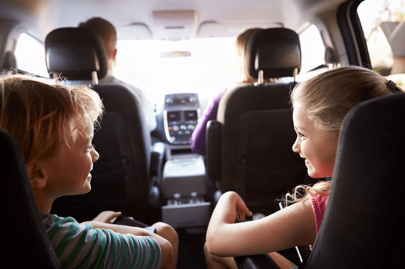 Deux enfants, un garçon et un fille, en train de rire à l'arrière d'une voiture.