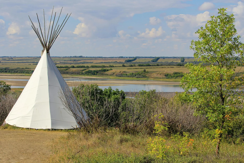 un tipi dans la verdure, près d'une rivière aux rives verdoyantes.
