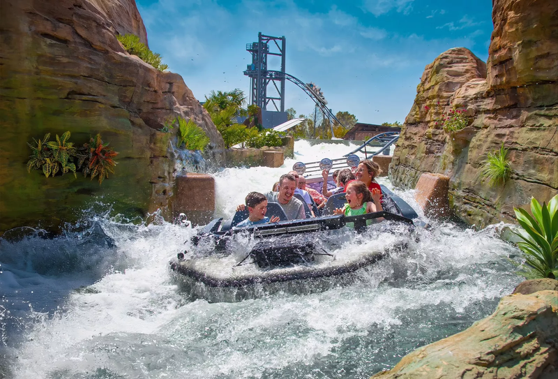Des enfants et des adultes dans un bateau sur un parcours d'eau vive dans un parc d'attractions.