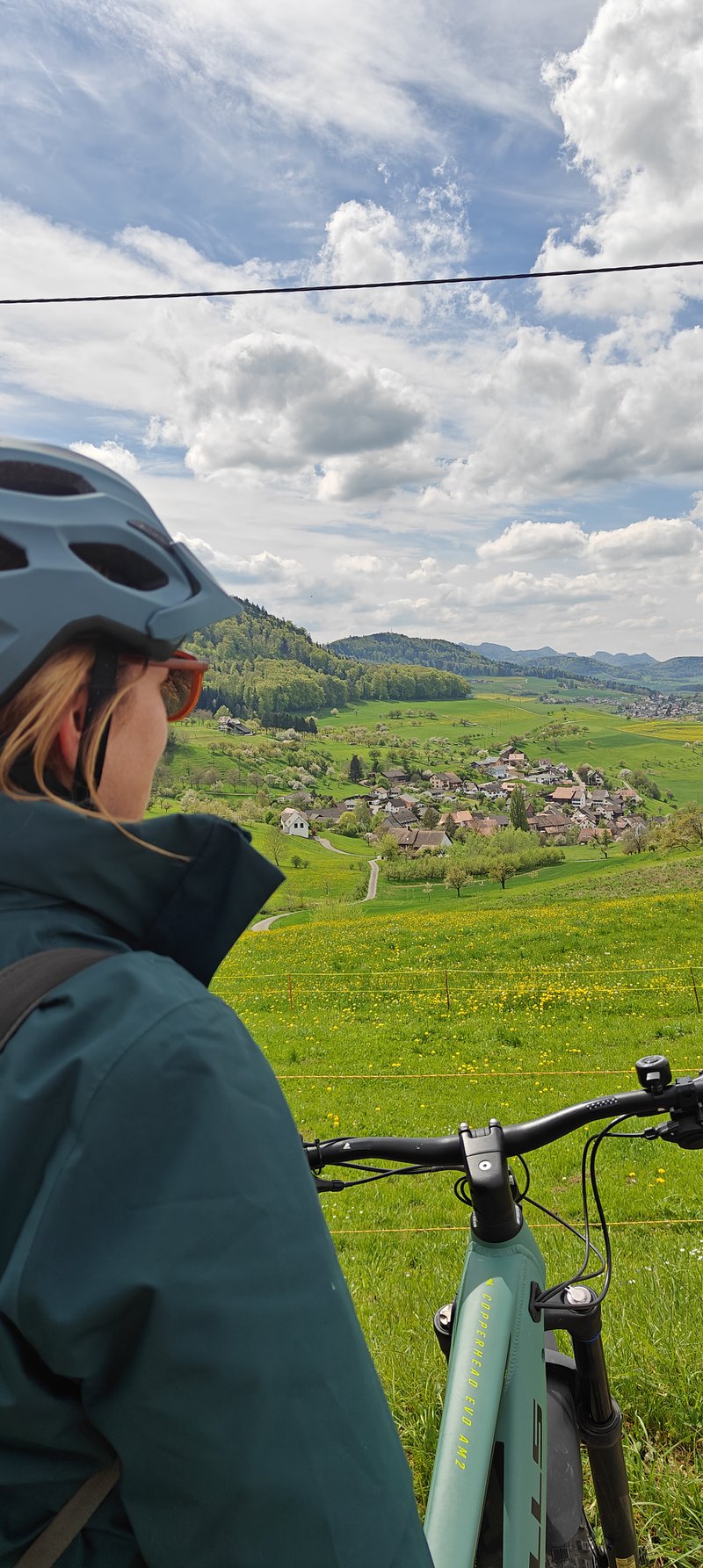 Jeune femme avec son vélo observant un paysage verdoyant en Suisse.