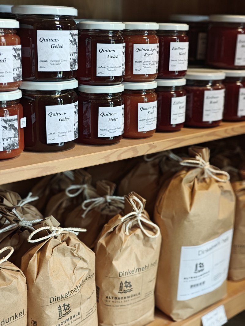 Pots de confitures artisanales et paquets de farine posés sur des étagères en bois.