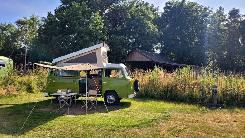 Camping: van aménagé installé dans un espace vert avec auvent, table et chaises devant.