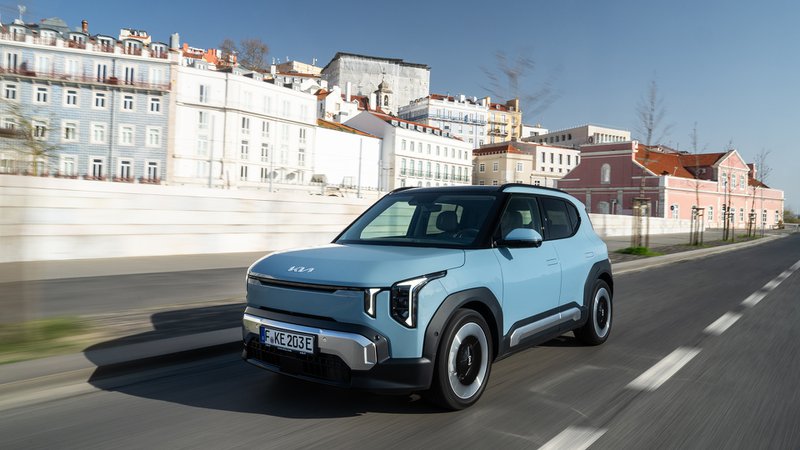 Kia EV2 bleu clair vue de trois quarts avant, en circulation dans un environnement urbain.