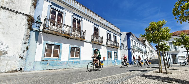 Alentejo, Portugal. Fietsers rijden over een straat met kinderkopjes langs witte huizen met blauwe accenten
