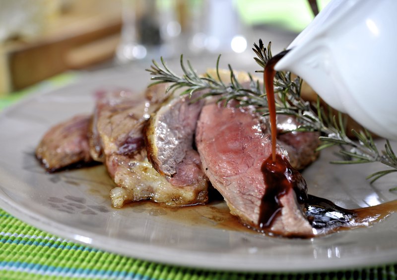 De la viande rôtie disposée en tranches sur une assiette et nappée de sauce