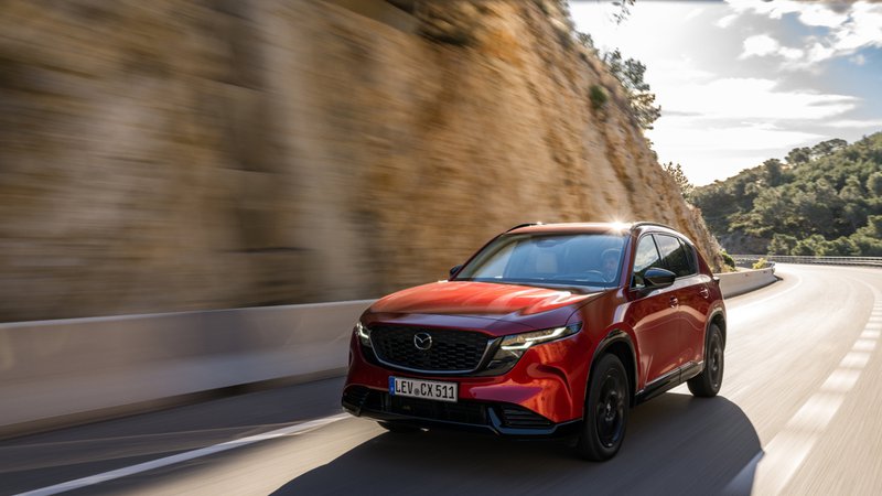 Mazda CX-5 rouge en mouvement sur une route sinueuse, vu de trois quarts avant.