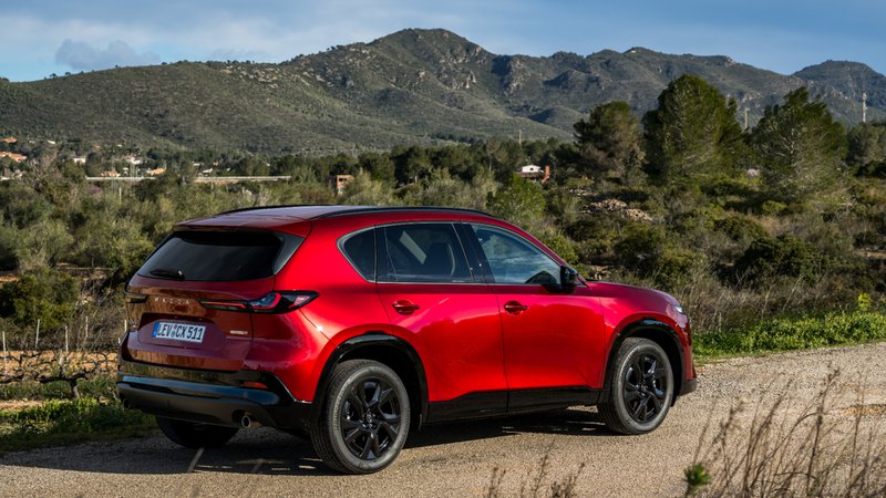 Mazda CX-5 rouge stationné dans un décor montagneux, vu de trois quarts arrière.