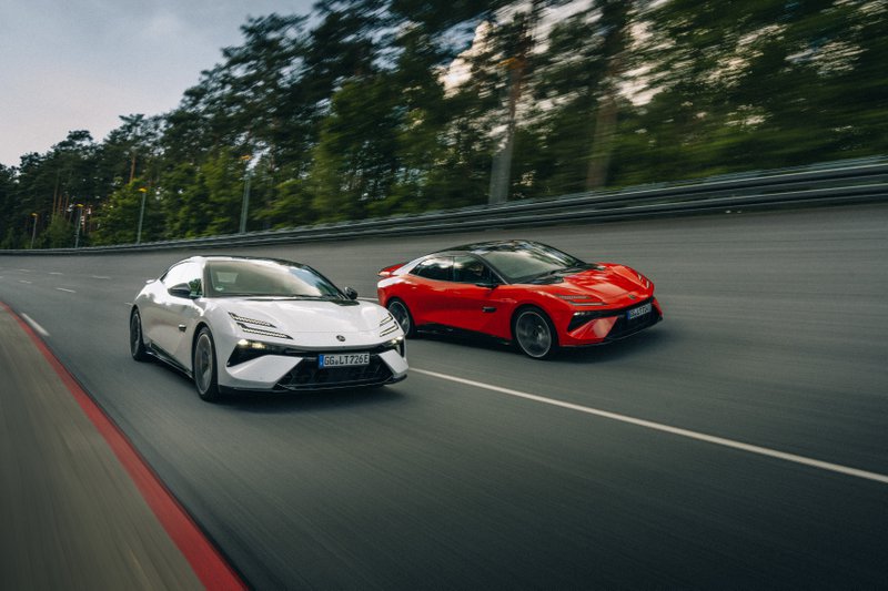 Deux Lotus Emeya électriques, une blanche et une rouge, roulant côte à côte sur une piste rapide entourée d’arbres.