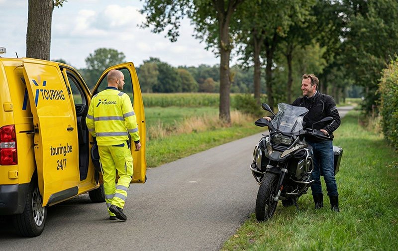 Touring wegenwachter arriveert bij motorrijder met lege batterij voor pechverhelping langs een landelijke weg in België