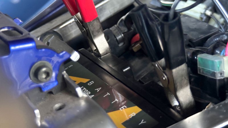 Close-up van motorbatterij met aangesloten druppellader klemmen op de polen