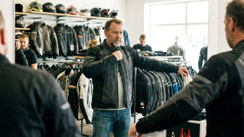 Un homme essaie une veste moto et teste l'ajustement dans le miroir d'un magasin spécialisé moto.